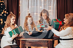 Children with mom and grandmother are sitting hugging on a large bed. Christmas mood. Against the background of a brick wall with