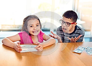 Children, money and cash for savings in home with conflict, jealousy and frustrated by table. Girl, boy and argument