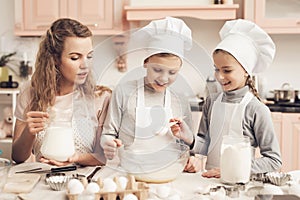 Children with mother in kitchen. Kids are adding flour and mother is adding milk in bowl.