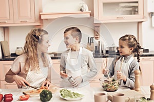 Children with mother in kitchen. Kids are helping mother to make salad.