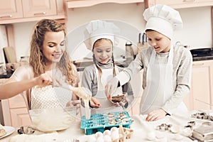 Children with mother in kitchen. Mother is putting dough in baking dish and kids are adding raisins.