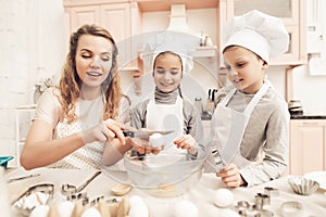 Children with mother in kitchen. Mother is teaching kids how to break eggs.