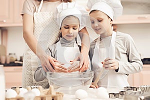 Children with mother in kitchen. Mother is teaching kids how to break eggs.