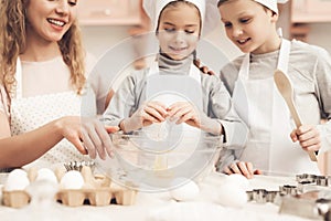 Children with mother in kitchen. Mother is teaching kids how to break eggs.