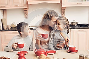 Children with mother in kitchen. Family is drinking tea with croissants.