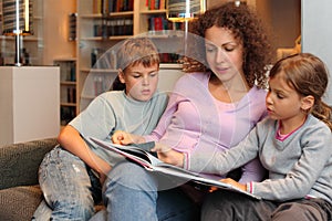 Children with mother sit on sofa and read book