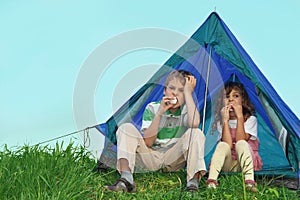 Children on nature, sit near tent and eat