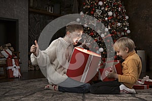 Children near Christmas tree with gift boxes. Two brothers open with New Years gifts. Kids opening Xmas presents