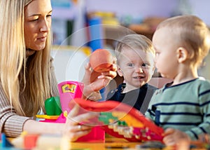 Children and nursery teacher play with toy scales in kindergarten playroom