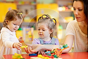 Children and nursery teacher play with toys in kindergarten playroom