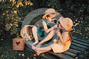 Children in overalls and straw hats eat pear while sitting on pallet