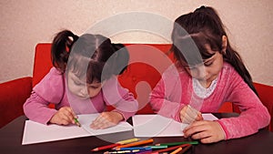 Children paint pencils. Two little girls draw on paper with crayons.
