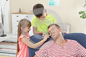 Children painting their father`s face while he sleeping