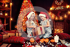 Children in pajamas in Santa& x27;s found presents near Christmas tree and now opening gift box