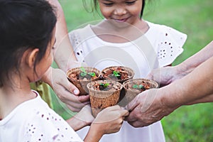 Children and parent hands holding young seedlings in recycle fiber pots together for planting in garden