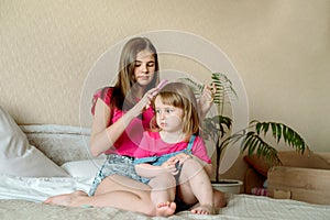 Children play on the bed in a bright bedroom. teen girl combing baby hair. funny girls. sisterly love. vacation home