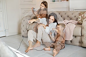 Children play on the console with their mother. The joy of passing a computer game. Mom son and daughter battle on the console