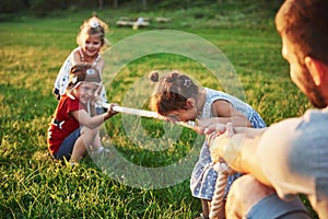 Children play with dad in the park. They pull the rope and have fun laying on a sunny day