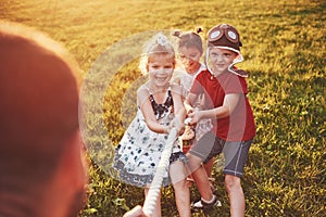 Children play with dad in the park. They pull the rope and have fun laying on a sunny day