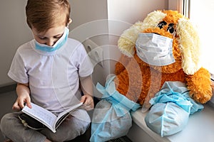 Children play a doctor. A large brown toy in a medical bandage and shoe covers is sitting on the window. A child is reading a book