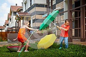 Children playing with garden sprinkler. Brother and sister running and jumping. Summer outdoor water fun in backyard