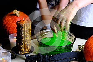 Children play with a green witchcraft potion, table is covered with a black cloth, pumpkins lie, animal skulls, candles are