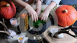 Children play with a green witchcraft potion, the table is covered with a black cloth, pumpkins lie, animal skulls, candles are