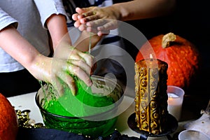 Children play with a green witchcraft potion, table is covered with a black cloth, pumpkins lie, animal skulls, candles are