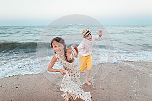 Children play and have fun on the beach. The girl and the guy run away from the waves