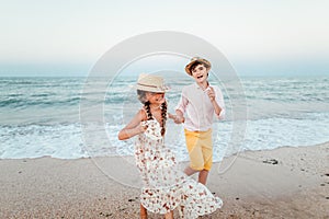 Children play and have fun on the beach. The girl and the guy run away from the waves