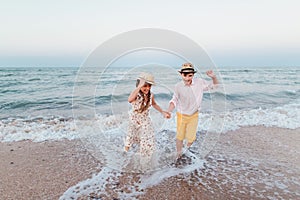 Children play and have fun on the beach. The girl and the guy run away from the waves