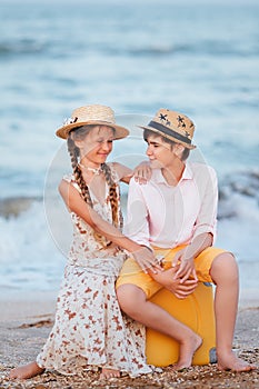 Children play and have fun on the beach. The girl and the guy run away from the wavesThe girl and the boy are sitting on a yellow