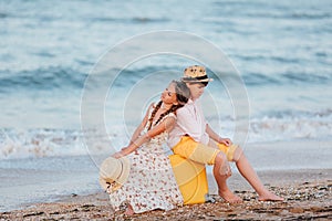 Children play and have fun on the beach. The girl and the guy run away from the wavesThe girl and the boy are sitting on a yellow