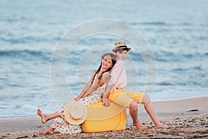 Children play and have fun on the beach. The girl and the guy run away from the wavesThe girl and the boy are sitting on a yellow
