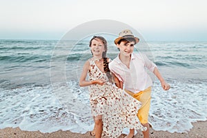 Children play and have fun on the beach. Romantic story on the seafront. The girl and the guy run away from the wave