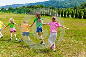 Children play holding hands on the green grass, back view