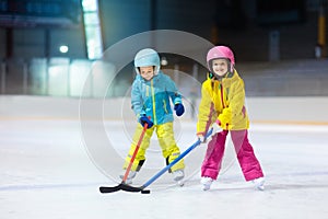 Children play ice hockey on indoor rink. Healthy winter sport for kids. Boy and girl with hockey sticks hitting puck. Child