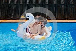 Children play on an inflatable swan ring in a pool.