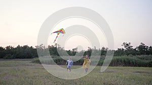 Children play with a kite, happy friends boy and girl run in clearing with an air toy enjoying fun on outdoor activities