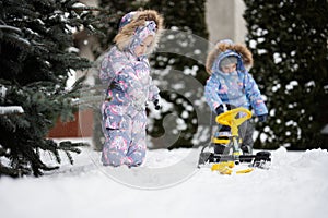 Children play outdoors in snow. Two little sisters enjoy a sleigh ride. Child sledding. Toddler kid riding a sledge. Kids sled in