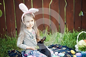 Children play with real rabbit. Laughing child at Easter egg hunt with white pet bunny. Little toddler girl playing with animal in