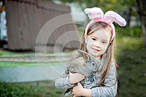 Children play with real rabbit. Laughing child at Easter egg hunt with white pet bunny. Little toddler girl playing with animal in
