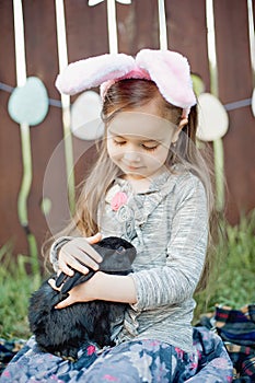 Children play with real rabbit. Laughing child at Easter egg hunt with white pet bunny. Little toddler girl playing with animal in