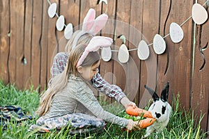 Children play with real rabbit. Laughing child at Easter egg hunt with white pet bunny. Little toddler girl playing with animal in