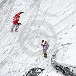 Children play in snow around cars in parking lot