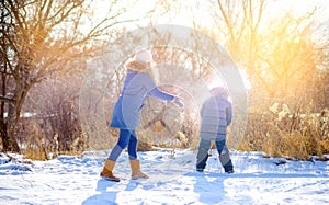 Children play in a snowy winter park at sunset. Throw snow and have fun.