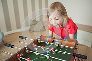 Children play table football in a children`s room, a little girl is worried and surprised