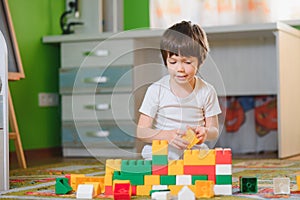 Children play with a toy designer on the floor of the children`s room. Boy playing with colorful blocks. Kindergarten educational