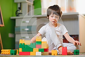 Children play with a toy designer on the floor of the children`s room. Boy playing with colorful blocks. Kindergarten educational