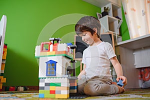 Children play with a toy designer on the floor of the children`s room. Boy playing with colorful blocks. Kindergarten educational